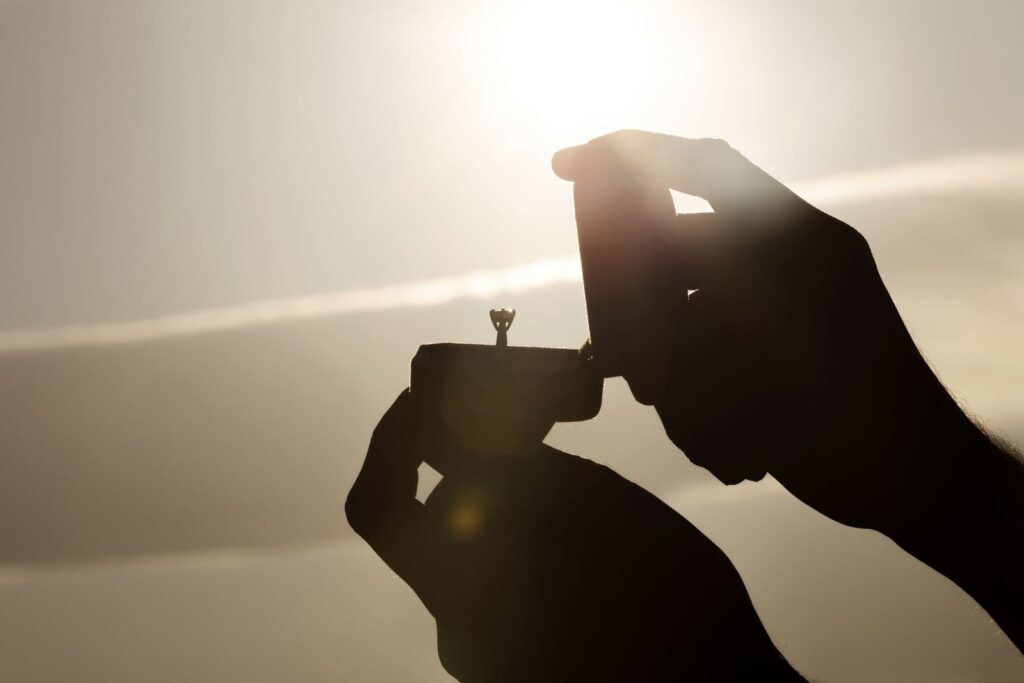 Hands holding an open engagement ring box against the sunset
