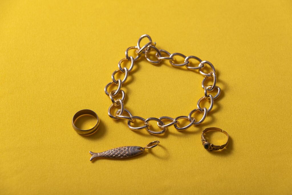 Gold chain bracelet and rings on a yellow background