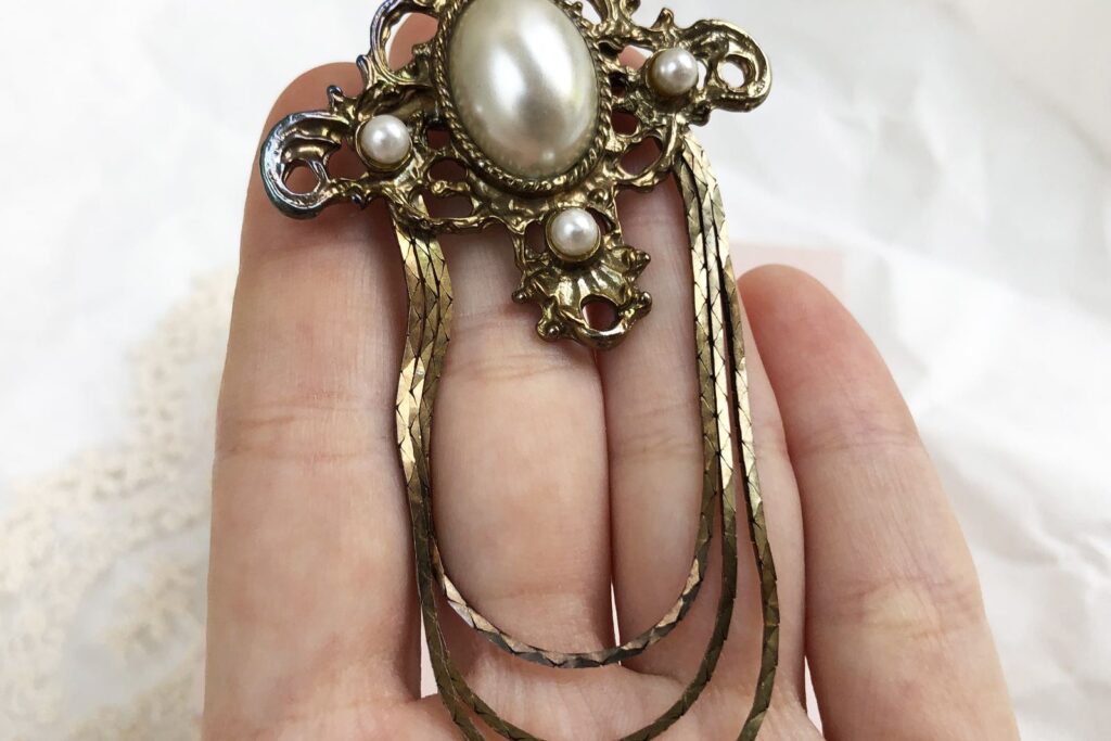 Vintage gold brooch with pearls held in a hand