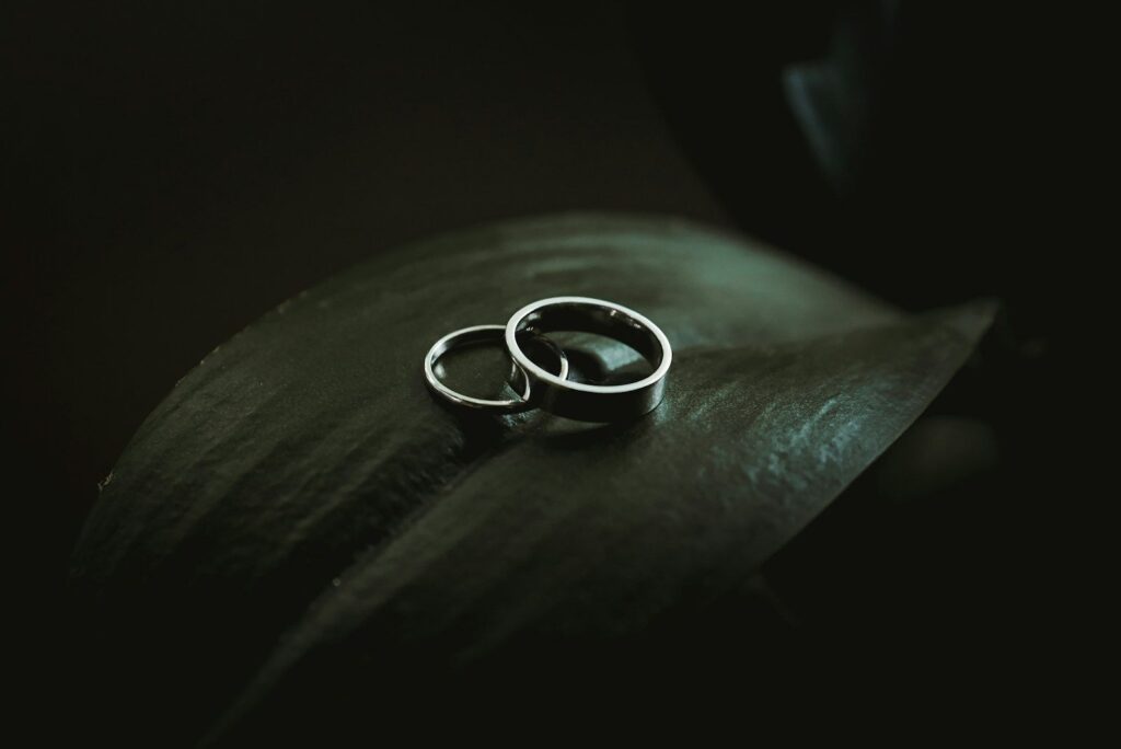 Two white metal wedding bands on a dark leaf