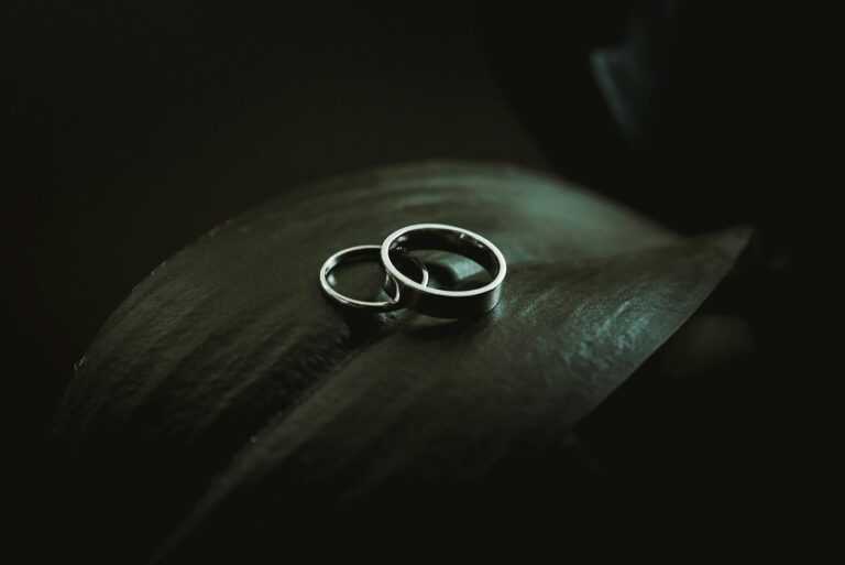 Two white metal wedding bands on a dark leaf